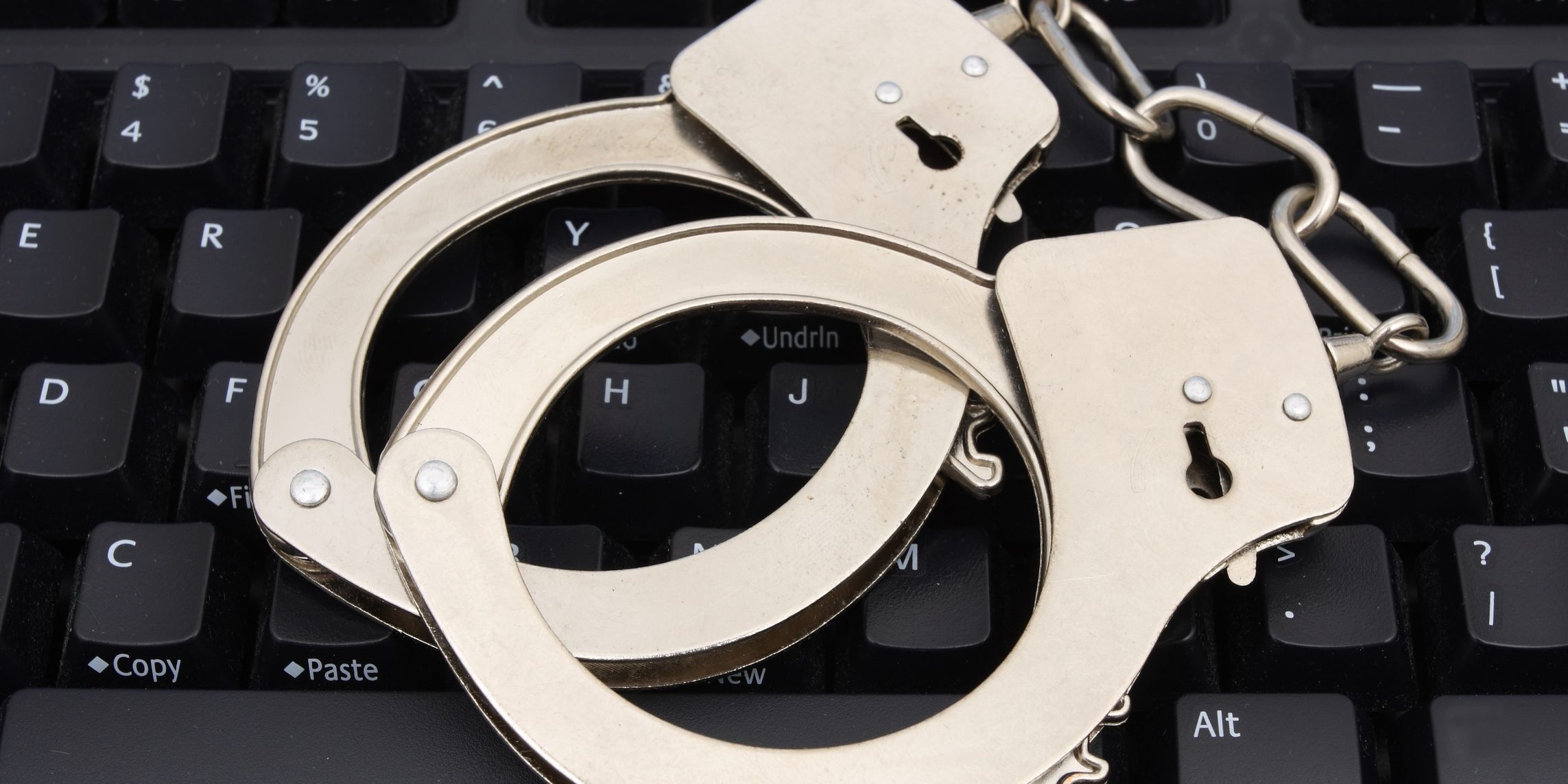 Handcuffs on computer keyboard for internet security کلاهبرداری
