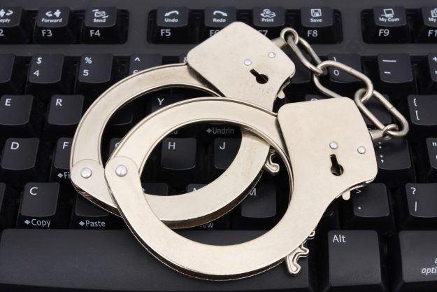Handcuffs on computer keyboard for internet security کلاهبرداری